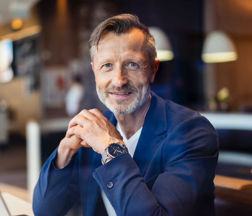 Klaus W. Reif sitting at a desk, dressed in a blue jacket with a silver wrist watch