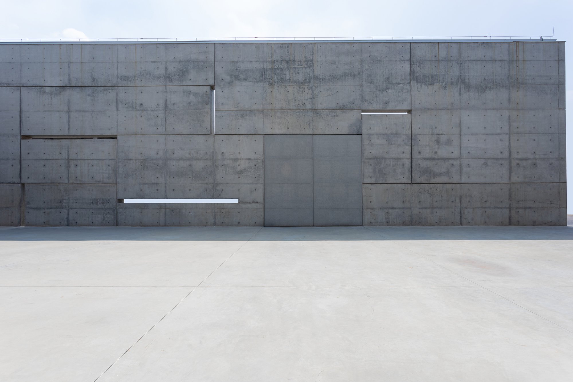 Modern concrete facade featuring a centered entrance and precise horizontal grid.